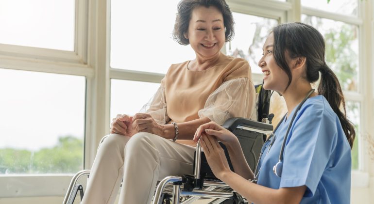 asian-young-caregiver-caring-her-elderly-patient-senior-daycare-handicap-patient-wheelchair-hospital-talking-friendly-nurse-looking-cheerful-nurse-wheeling-senior-patient asian young caregiver caring for her elderly patient at senior daycare Handicap patient in a wheelchair at the hospital talking to a friendly nurse and looking cheerful nurse wheeling Senior patient