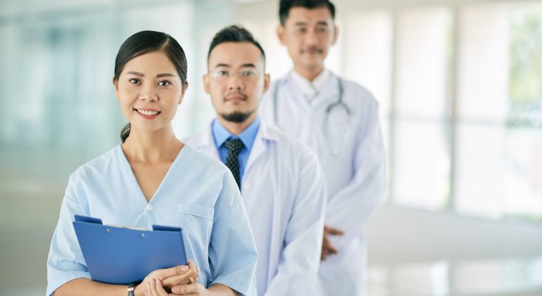 Pretty female doctor Portrait of pretty Vietnamese female doctor and her coworkers behind