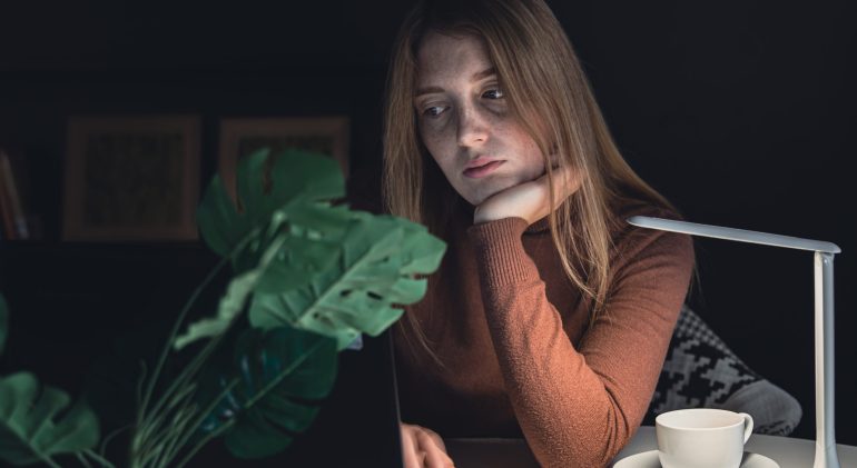 A young woman works behind a laptop at night with a lamp light. adolescent depression and social media